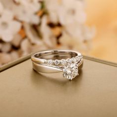 two wedding rings sitting on top of a box with flowers in the backgroud