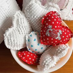 a bowl filled with red and white knitted hearts on top of a wooden table