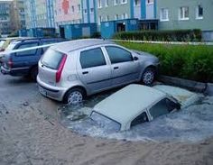 two cars are submerged in the water near some buildings and bushes on a city street