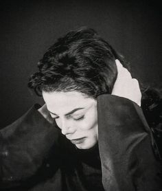 a black and white photo of a woman with her hands on her head, looking down