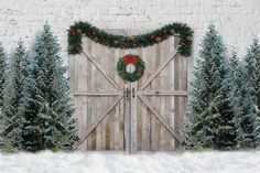 christmas wreaths are hanging on the wooden door to an old barn with snow and evergreen trees