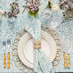 a place setting with plates, silverware and flowers on a blue table cloth covered table