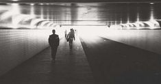 black and white photograph of two people walking in a tunnel with light at the end