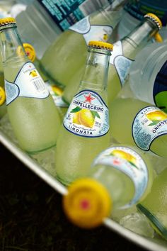 several bottles of lemonade sitting on top of a metal tray filled with water and lemons