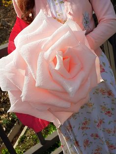 a woman holding a large pink rose in her hand