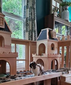 a cat sitting on top of a wooden table next to a doll house and window