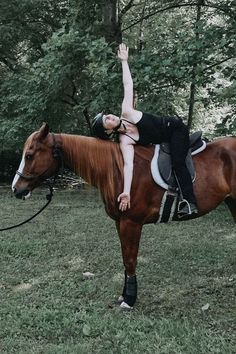 a woman riding on the back of a brown horse in a field next to trees