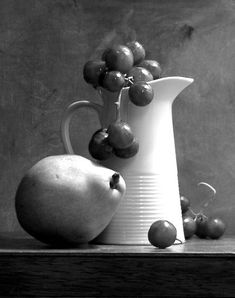 black and white photograph of fruit in front of a pitcher on a table with grey background