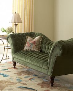 a green couch sitting on top of a rug in a living room next to a window