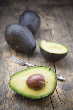 an avocado cut in half on top of a wooden table with two forks