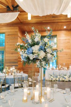 a tall vase filled with white and blue flowers sitting on top of a table covered in candles