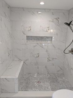 a bathroom with white marble walls and floor, shower head, and bench in the corner