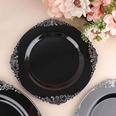 three black and silver plates with flowers on the table next to them, one is empty