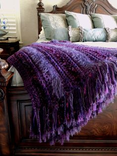 a bed with a purple blanket on top of it next to pillows and pillow cases