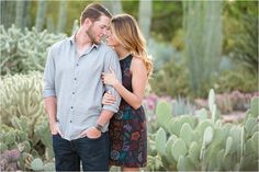 a man and woman standing next to each other in front of cacti plants