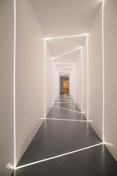 an empty hallway with white walls and light at the end is lit by neon lights