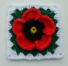 a crocheted square with a red flower on the center and green leaves in the middle