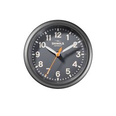 a black clock with orange hands on a white background and the words shinola written below it