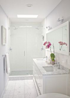 a white bathroom with two sinks and a walk in shower next to a toilet that has pink flowers on the counter