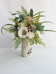 a vase filled with flowers and greenery sitting on top of a table next to a white wall