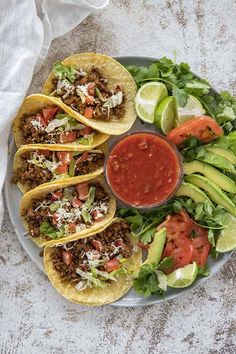 three tacos on a plate with lettuce, tomato and avocado