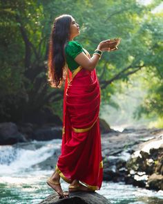 a woman in a red and green sari standing on rocks next to a river