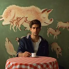 a man sitting at a table in front of a wall with animals painted on it