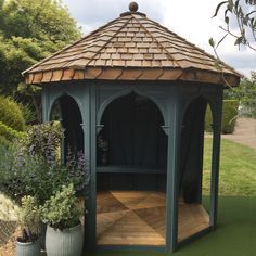 a wooden gazebo sitting in the middle of a lush green field with potted plants