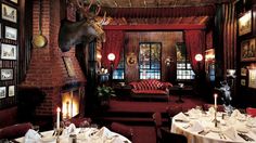 a restaurant with tables and chairs in front of a fire place that has an elk head on the wall