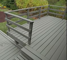 a wooden deck with metal railings in front of some bushes and flowers on the other side