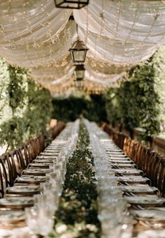 the long table is set with clear glassware and place settings for guests to sit at