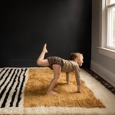 a little boy that is standing on one leg in front of a rug and looking at the ground