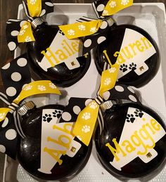 four black and white ornaments with yellow ribbon in a box on top of a table