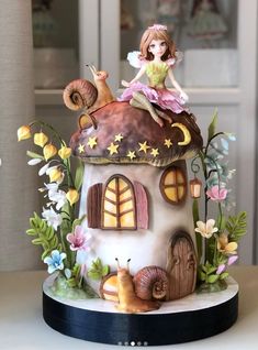 there is a cake that looks like a house with a fairy sitting on the roof