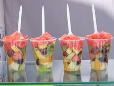 four plastic cups filled with different types of fruit on top of a glass countertop