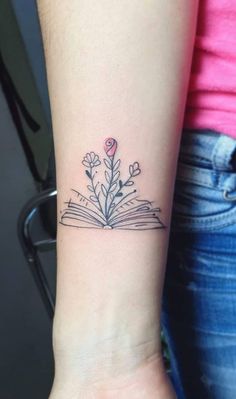 a small tattoo on the wrist of a woman with an open book and flowers in it