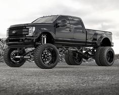 a large black truck parked on top of a dirt field