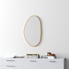 a white dresser topped with books and a round mirror on the wall above it's head