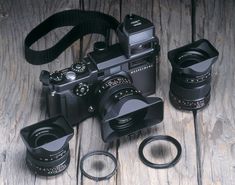 an old camera and two new lenses on a wooden table with a strap around it