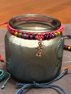 a glass jar sitting on top of a table covered in colorful beads and string bracelets