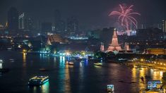 fireworks are lit up in the night sky over a river with boats and large buildings