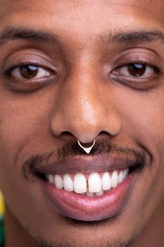 a close up of a man with a nose ring on his nose smiling at the camera