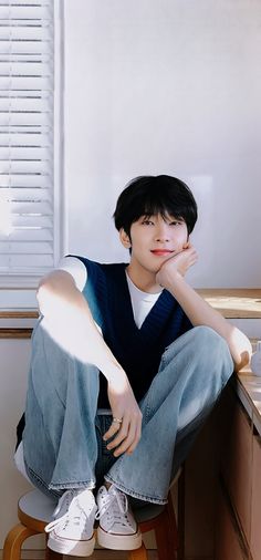 a young man sitting on top of a wooden chair next to a desk with his hand under his chin