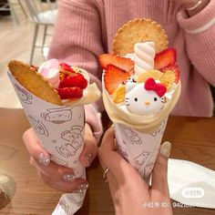 two ice cream cones with strawberries and hello kitty toppings are held up to the camera