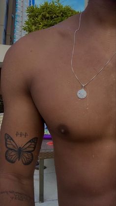 a shirtless man with a butterfly tattoo on his arm and chest, standing in front of a building