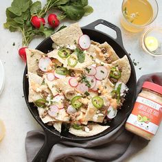 a skillet filled with nachos and veggies next to glasses of orange juice