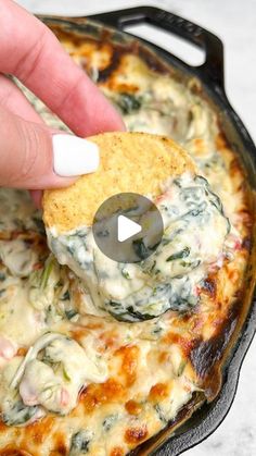 a hand dipping a piece of bread into a skillet filled with spinach and cheese