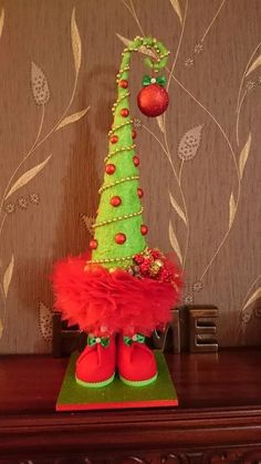 a small christmas tree with red and green decorations on it's head, sitting on top of a wooden shelf