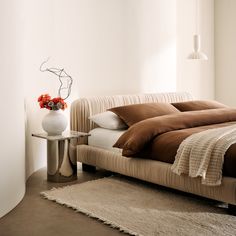 a bed with brown and white comforters in a bedroom next to a vase filled with flowers