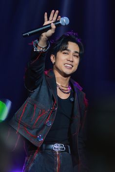 a male in a black shirt is holding a microphone and smiling at the camera while standing on stage